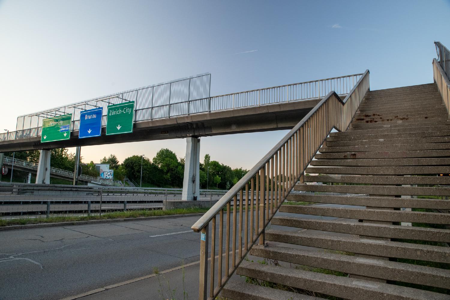 Stairs going up a bridge above the Autobahn. Direction signs to Zürich are visible.