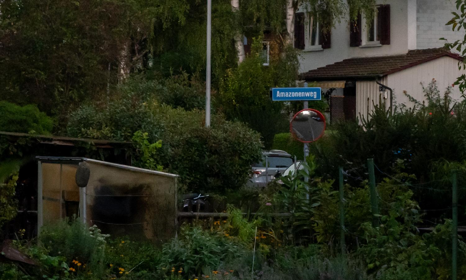 A blue Amazonenweg street sign in front of a house, in an area with a lot of greenery.