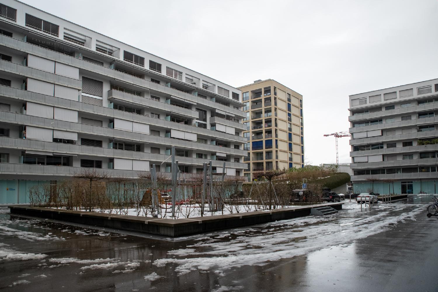 A playground covered with snow, in the yard between 8-story residential buildings.