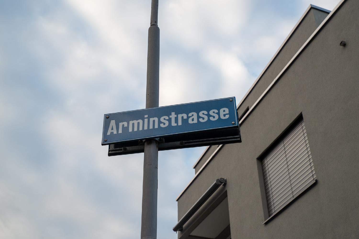 A blue "Arminstrasse" sign on a metallic pole in front of a building.