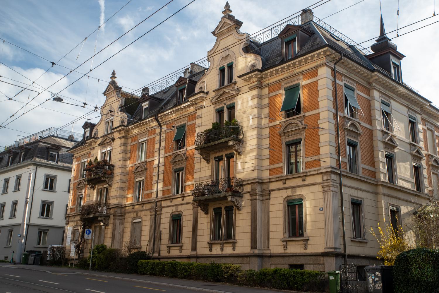 A cream and brown 4-story residential building with arched dormers and a spire